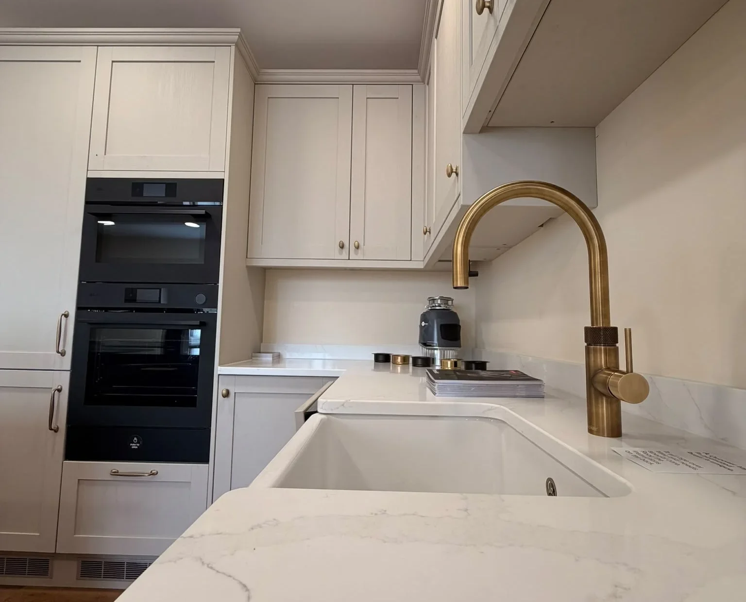 Belfast sink with a brushed brass tap and marble-effect quartz worktop in a cream shaker kitchen
