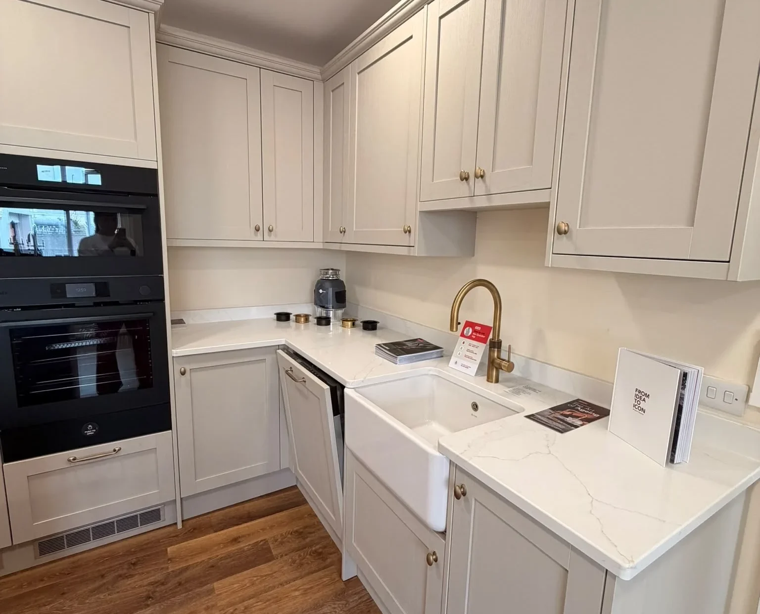 Cream shaker kitchen with built-in ovens, a Belfast sink and a brass tap in the Bristol showroom