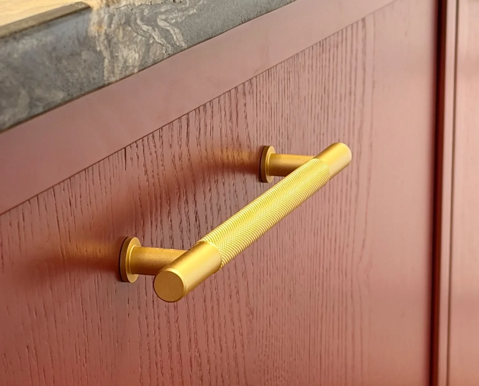 Knurled brass bar handle on a red oak shaker kitchen door under a marble worktop