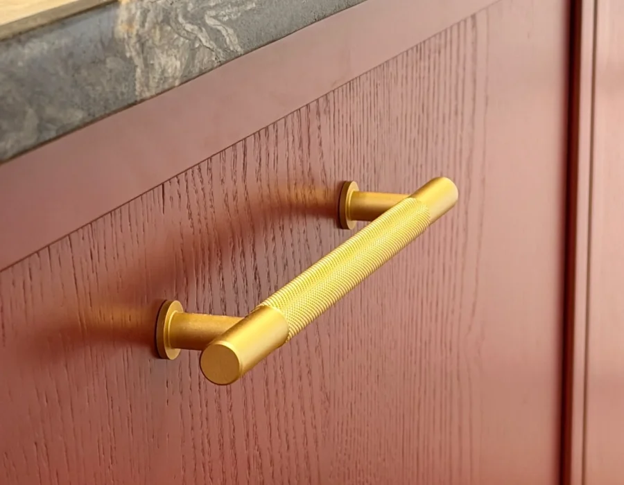 Knurled brass bar handle on a red oak shaker kitchen door under a marble worktop
