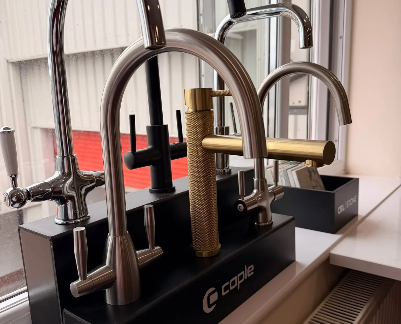 Caple kitchen tap display with chrome, black and brass mixer taps in the showroom window