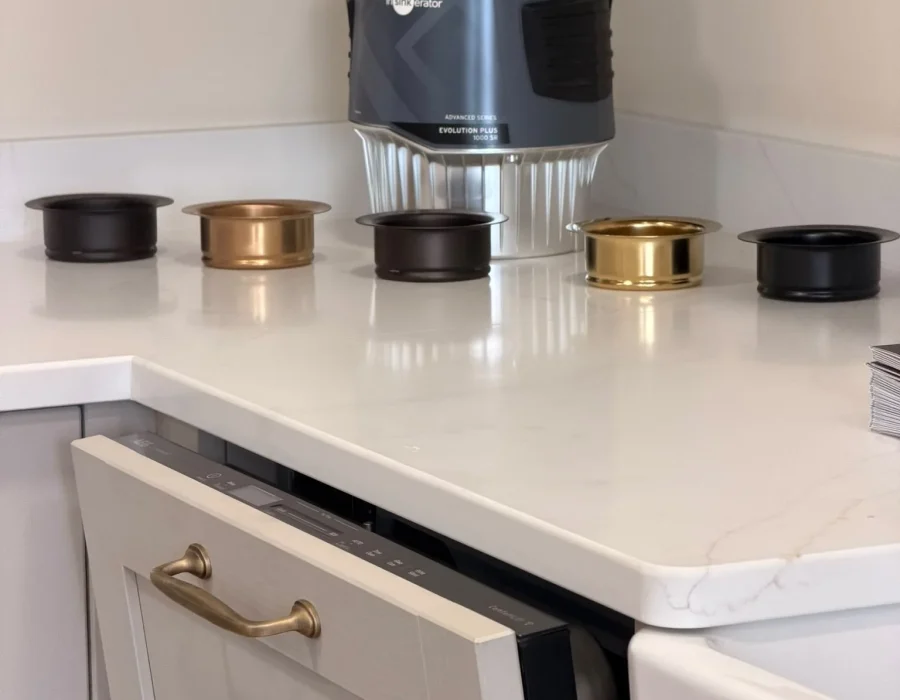InSinkErator waste disposal unit with sink flanges in brass, chrome and black on a quartz worktop