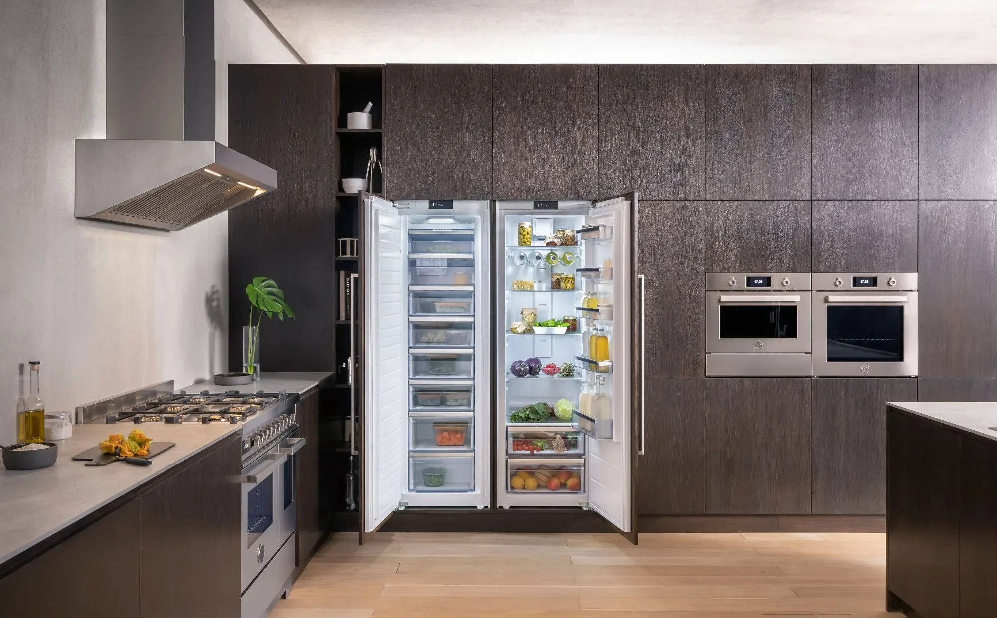 Integrated fridge and freezer columns side by side in a dark wood kitchen with built-in ovens